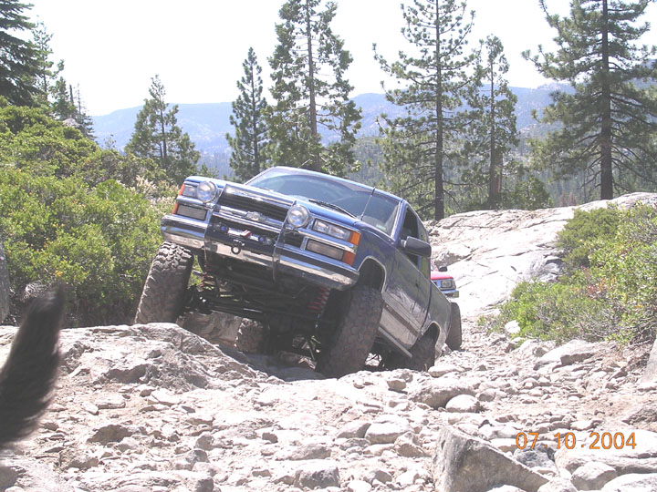 Dark blue lifted Chevy pickup with brush guard crawling granite rocks on a mountain trail