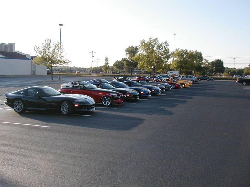 Black Dodge Viper coupe leading a row of parked sports cars in a lot