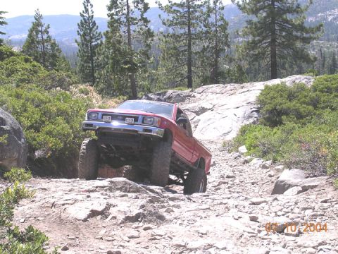 1994 Ford Bronco - A red pickup truck navigates a challenging rocky terrain in a mountainous, wooded area.