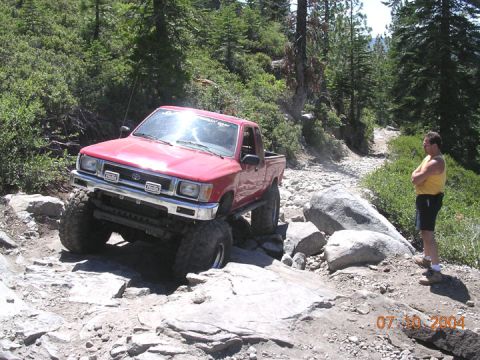 1994 Ford Bronco - A red 1994 Toyota pickup truck tackles a challenging rocky trail, with a man observing from the side.