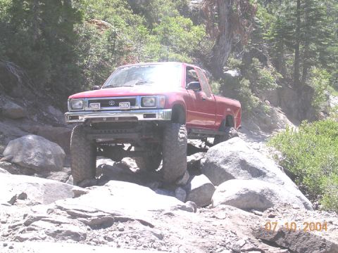 1994 Ford Bronco - A red Toyota pickup truck is shown navigating a challenging rocky terrain on a sunny day.
