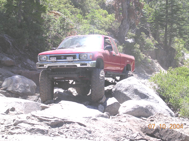 red Toyota pickup truck with large tires navigating a rocky trail