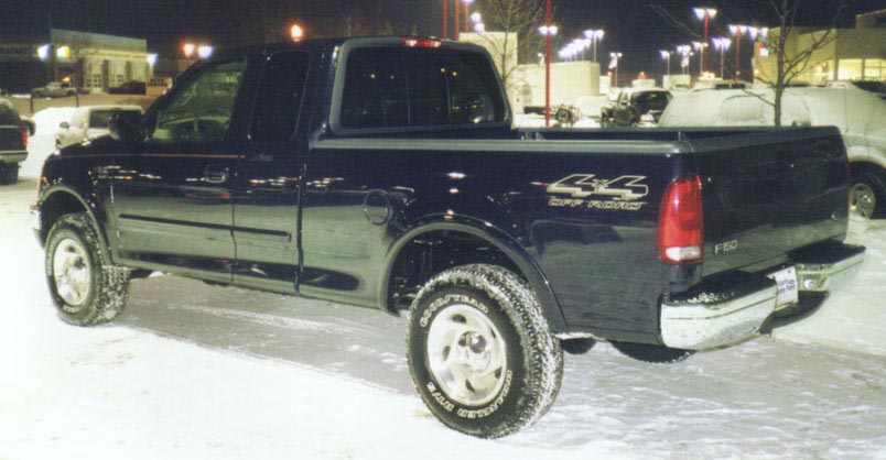 Dark blue Ford F-150 4x4 extended-cab pickup, rear three-quarter view, in snowy lot at night