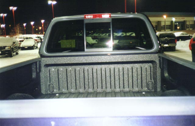 Pickup truck bed with spray-in liner and rear cab window at night