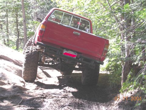 1994 Ford Bronco - A red pickup truck navigates a challenging off-road trail with steep inclines and loose terrain.