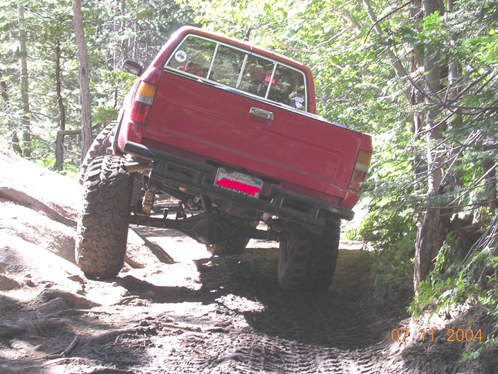 Red lifted compact pickup flexing rear suspension on an off-camber forest trail