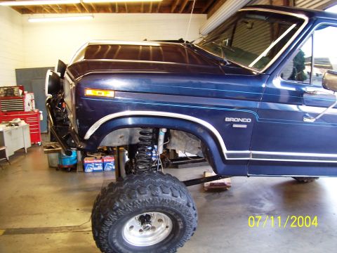 1985 Ford Bronco - A blue Ford Bronco is shown in a garage with its suspension lifted and large tires installed.