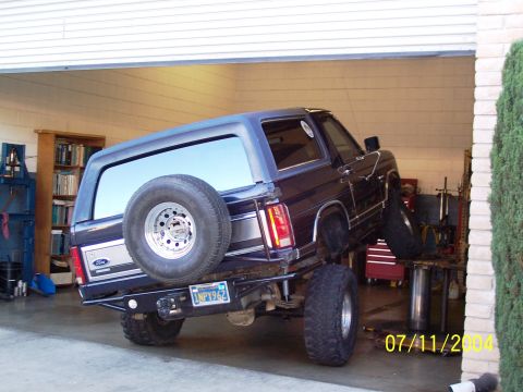 1985 Ford Bronco - Ford Bronco is raised on a lift inside a garage, with a spare tire mounted on the back.