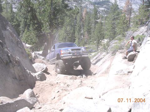 1994 Ford Bronco - A lifted pickup truck navigates a rocky off-road trail with a person watching from the side.