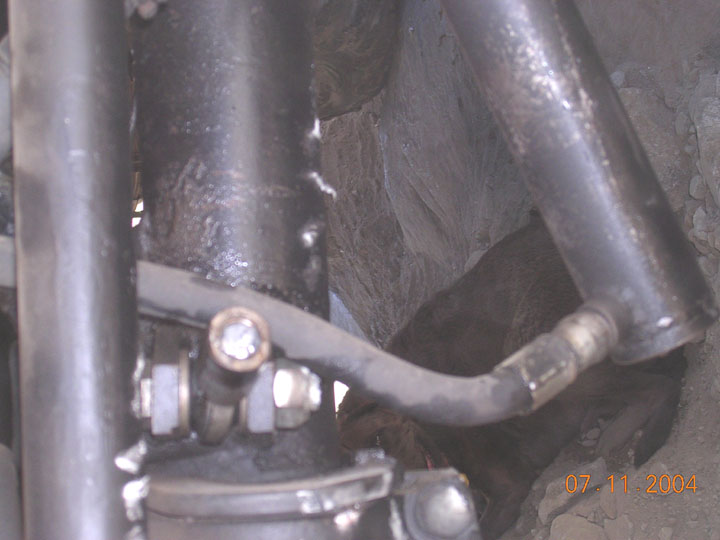 Hydraulic ram-assist steering cylinder and hose mounted to a greasy solid axle
