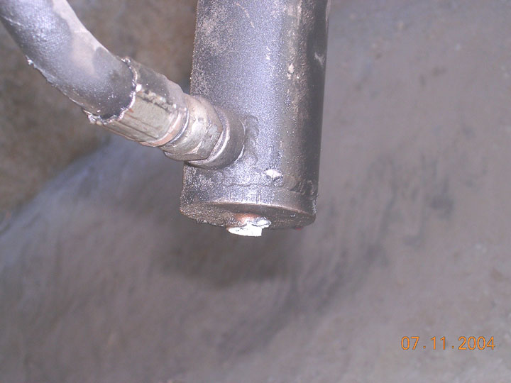 Close-up of a hydraulic cylinder body with a welded port fitting and steel line