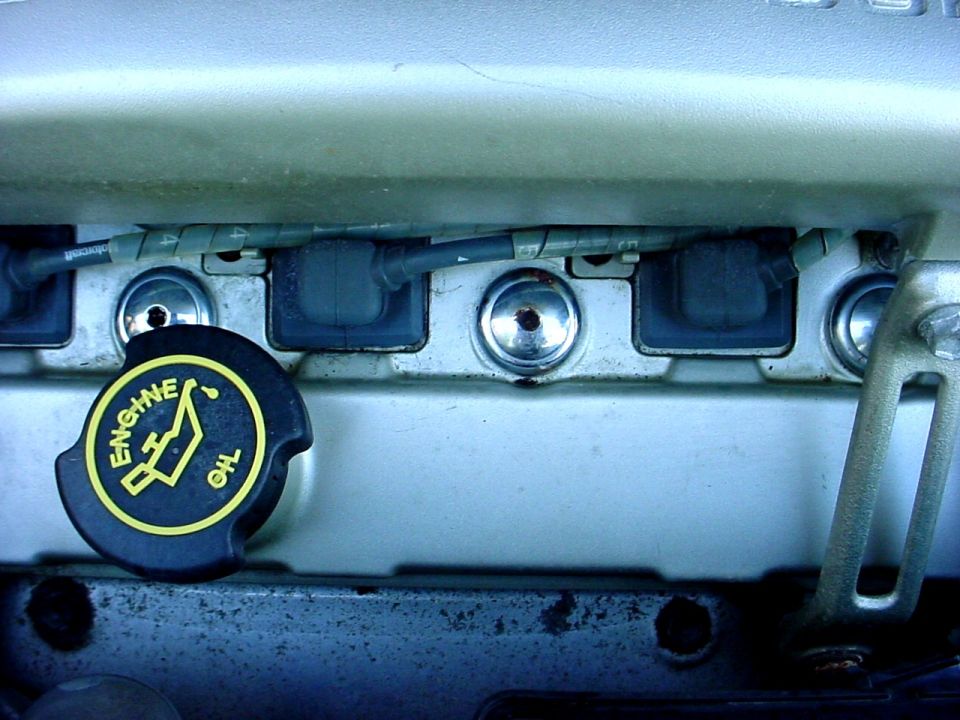 Black engine oil cap with yellow text and symbol, next to spark plug wires
