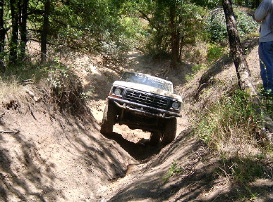 1978 Ford Bronco - A 1978 Ford Bronco tackles a challenging off-road trail, its tires kicking up mud as it descends into a ditch.