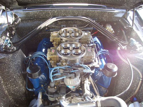 Engine bay with dual Holley carburetors, blue spark plug wires, and a chrome strut tower brace