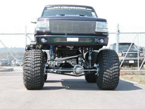 1994 Ford Bronco - This heavily modified pickup truck features an extreme lift kit and oversized tires, with a custom grille and a website banner on the winds…