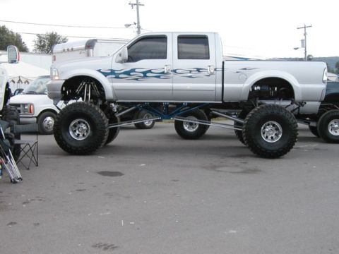 1994 Ford Bronco - A heavily modified silver pickup truck with custom flame decals and massive tires is parked outdoors.
