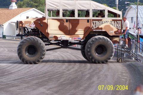 1979 Ford Bronco - A modified monster truck with camouflage paint and large tires is parked on a paved surface.