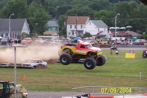 1979 Ford Bronco - Monster truck jumps over destroyed cars at an event with spectators watching.