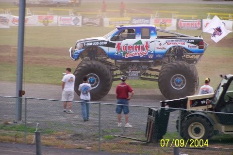 1979 Ford Bronco - A monster truck with "Summit Truck Style" branding is parked on a dirt lot with spectators nearby.