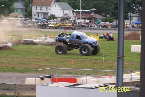 1979 Ford Bronco - A monster truck is in action at an outdoor event, with cars being crushed in the background.