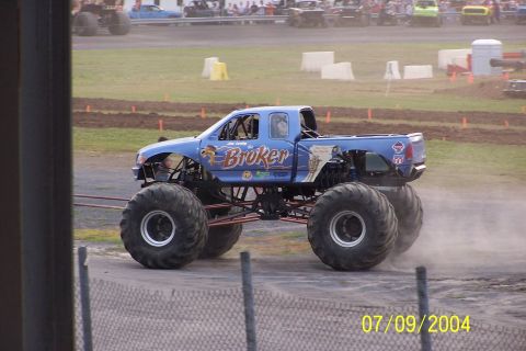 1979 Ford Bronco - A blue monster truck with "Broker" written on the side drives on a dirt track, kicking up dust.