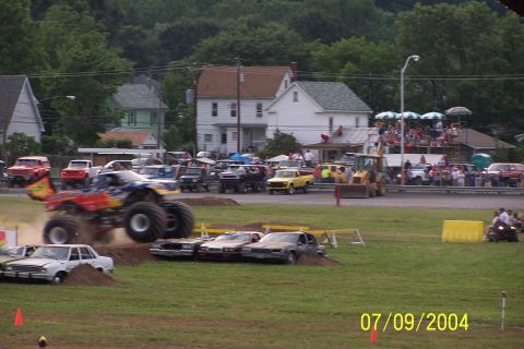 1979 Ford Bronco - A monster truck soars through the air over a line of cars during an event.