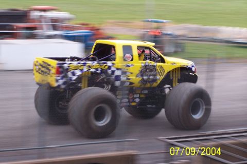 1979 Ford Bronco - A yellow monster truck with custom graphics drives on a dirt track.