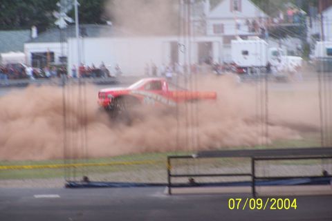 1979 Ford Bronco - A red pickup truck races through dirt, creating a massive dust cloud during an event.