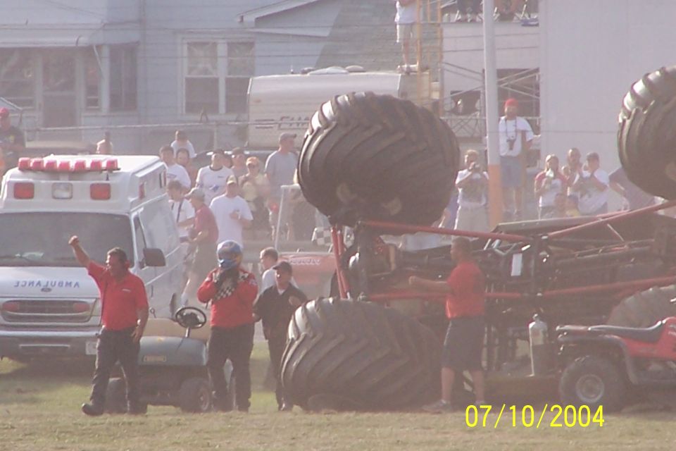 Monster truck with large tires and red frame, an ambulance, and ATVs on a dirt field