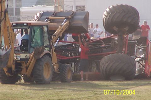 1979 Ford Bronco - A backhoe is used to lift a monster truck, which has extremely large tires, at an outdoor event.