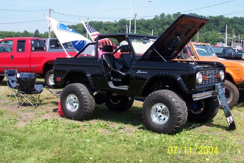 1979 Ford Bronco - A black Ford Bronco is displayed with its hood open, alongside other vehicles at an outdoor event.