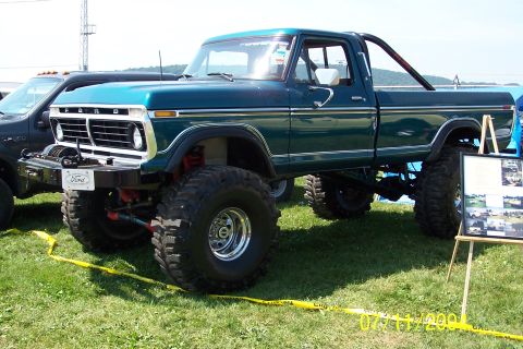 1979 Ford Bronco - This lifted Ford pickup truck features a prominent grille and large off-road tires, parked on grass with a display board nearby.