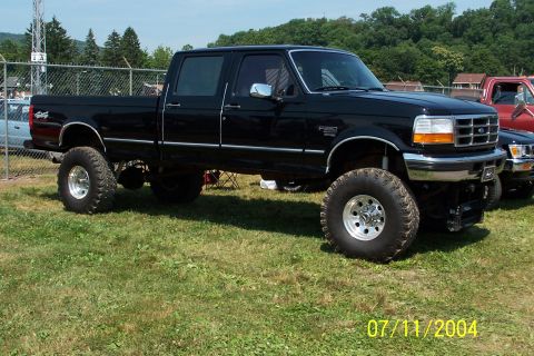 1979 Ford Bronco - A lifted black Ford F-250 pickup truck is parked on grass next to another vehicle.