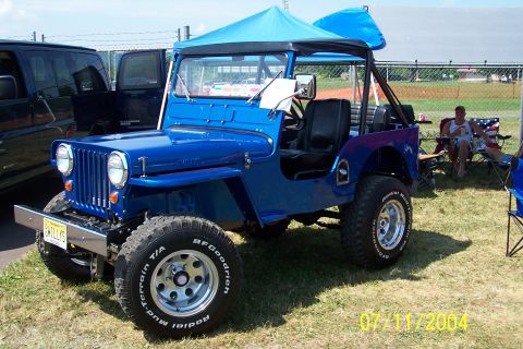 1979 Ford Bronco - A bright blue Jeep is parked on grass with a blue canopy overhead and a dark SUV to its left.