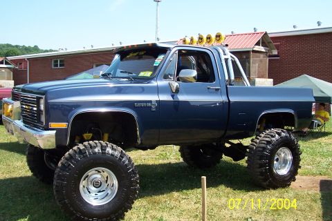 1979 Ford Bronco - A lifted blue pickup truck with a chrome grille and large tires sits on a grassy field.