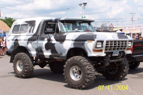 1979 Ford Bronco - This lifted pickup truck features a unique camouflage paint job and a camper shell, parked outdoors.