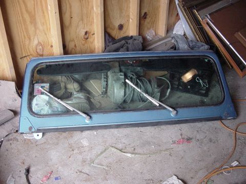 1992 Ford Bronco - A detached blue rear window assembly sits on a concrete floor in front of a wooden wall.