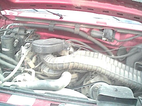 1994 Ford Bronco - The engine bay of a red vehicle is shown, various hoses and the air intake system.
