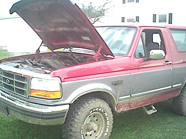 Red and gray Ford Bronco with hood open, showing engine. Mud on lower body panels