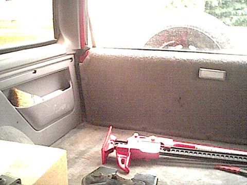 1994 Ford Bronco - Vehicle interior with a jack and a brush; spare tire visible through the rear window.