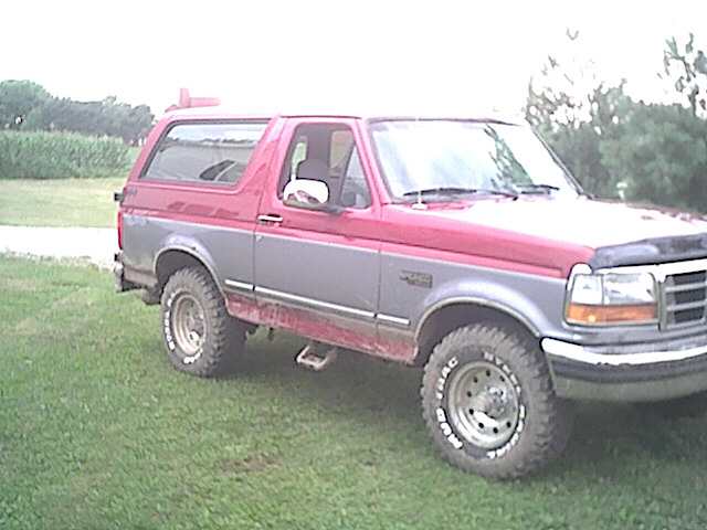 Red and gray Ford Bronco parked on grass. Has aftermarket wheels and tires