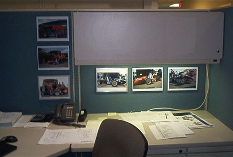 1985 Ford LTD Crown Victoria - A desk in an office cubicle displays framed photographs of race cars on the wall above the workspace.