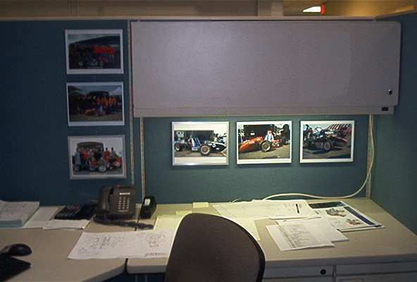 Office cubicle wall with framed photos of race cars and a whiteboard