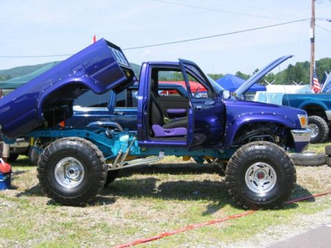 1994 Ford Bronco - This heavily modified Toyota pickup truck features a custom paint job and lifted suspension, with its bed and doors open.