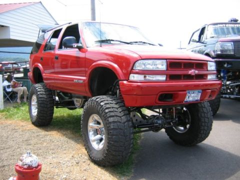 1994 Ford Bronco - Lifted red Chevrolet Blazer parked outdoors next to another modified truck.