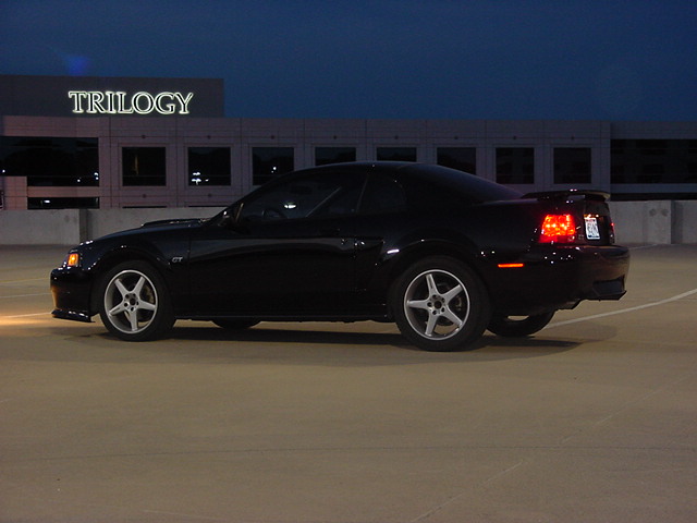 Black Ford Mustang GT coupe parked at dusk on a parking garage rooftop near a TRILOGY sign