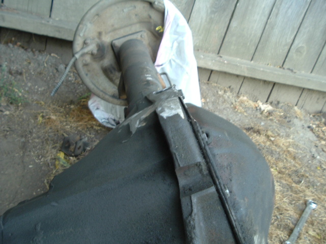 Removed rear axle with brake drum and black differential housing on the ground by a wood fence