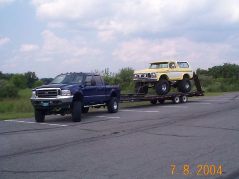 1978 Ford Bronco - A yellow and white 1978 Ford Bronco is transported on a trailer pulled by a blue Ford pickup truck.