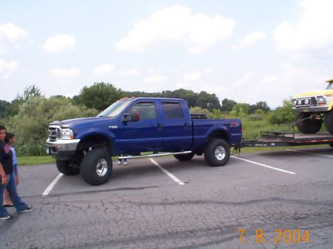 1978 Ford Bronco - Blue Ford F-250 Super Duty towing a yellow Ford Bronco on a trailer in a parking lot.