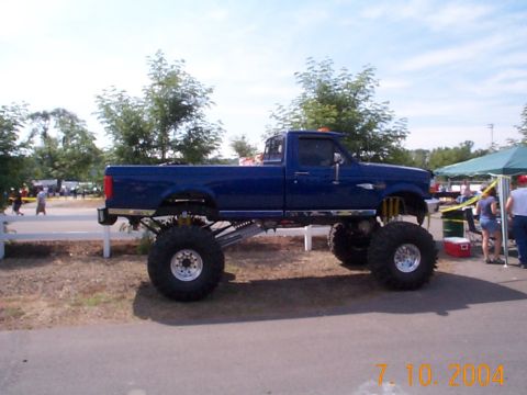 1978 Ford Bronco - A heavily modified pickup truck with oversized wheels and a raised suspension is displayed at an outdoor event.
